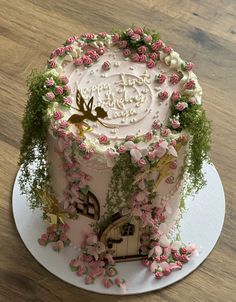 a cake decorated with pink flowers and greenery on a white plate sitting on a wooden table