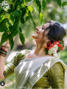 a woman in a green and white sari holding flowers up to her face while smiling