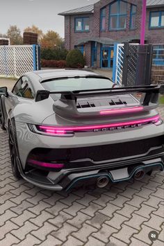 a grey sports car parked in front of a house with pink lights on the hood