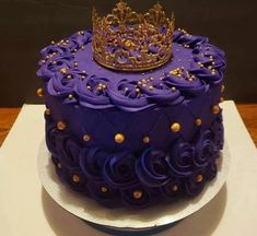 a purple cake with gold decorations and a crown on top is sitting on a white plate