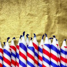 several candles with blue and red stripes are lined up on a gold cloth, some have birds perched on them