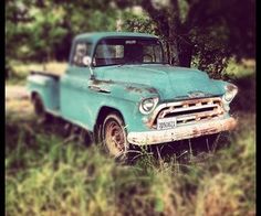 an old blue truck is parked in the grass