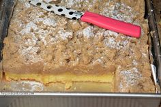 a cake with powdered sugar on top and a pink knife in the middle, sitting in a metal pan