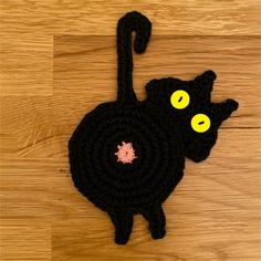 a crocheted black cat with yellow eyes sitting on top of a wooden floor