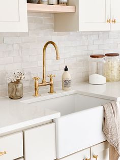 a white kitchen with gold faucet and brass handles on the sink countertop