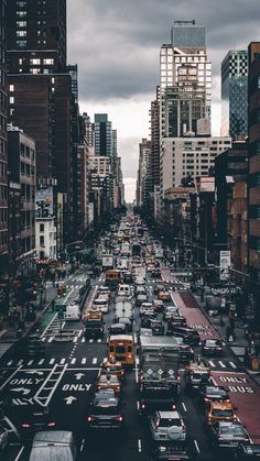 a city street filled with lots of traffic and tall buildings under cloudy skies in the distance