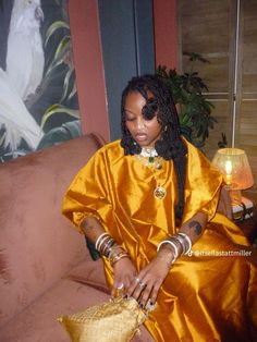 a woman sitting on top of a couch wearing an orange dress and gold bracelets