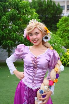 a woman in a purple dress with flowers on her head is holding a stuffed animal