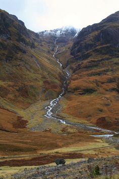 the mountains are covered in snow and brown grass, with a stream running between them