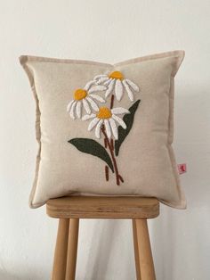 a white pillow with daisies on it sitting on a wooden stool next to a wall