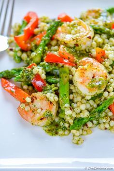 a white plate topped with vegetables and shrimp on top of couscouse next to a fork