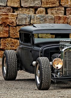 an old model car is parked in front of a brick wall