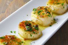 three scallops on a white plate with parsley sprinkled on top