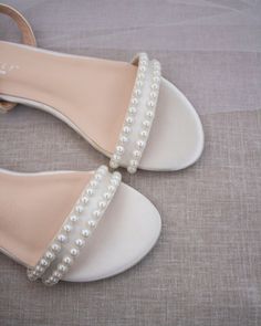 a pair of white shoes with pearls on the toe and heel are sitting on a bed