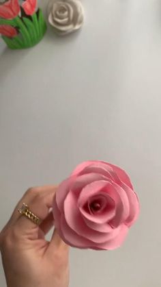 a person holding a pink flower in front of a white table with flowers on it