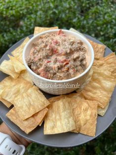 a person holding a plate with chips and salsa in the middle, on top of it