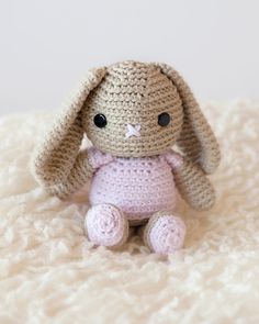 a pink crocheted stuffed animal sitting on top of a blanket in the shape of a bunny