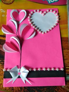 a pink card with white hearts and pearls on the side, sitting on top of a table