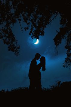 a man and woman standing under a tree at night with the moon in the background