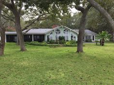 a white house surrounded by trees in the middle of a grassy area with lots of green grass