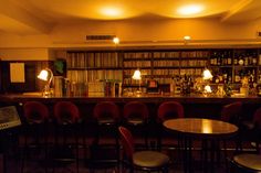 a dimly lit bar with red chairs and bookshelves in the back ground area