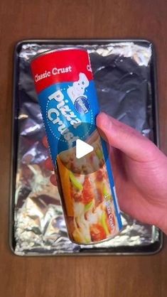 a hand holding a can of food in front of tin foil on a wooden table