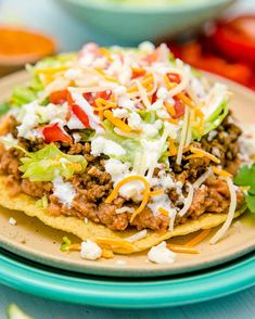 a plate with some taco salad on it and other food items in the background