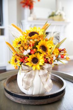 a white pumpkin decorated with sunflowers and feathers on top of a wooden tray