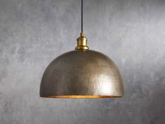 a large metal dome light hanging from a wire on a gray wall with concrete background