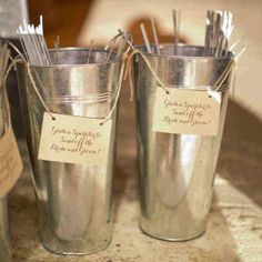 two silver buckets with sticks in them sitting on a table next to each other