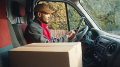 a man driving a truck with a cardboard box on the front seat and his hand on the steering wheel