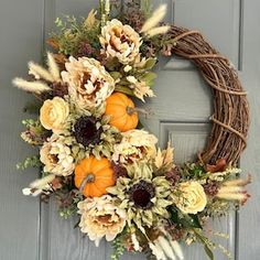 a wreath with flowers and pumpkins hanging on the front door to decorate it for fall