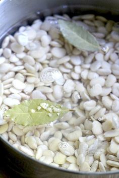 a pot filled with white beans next to a green leaf