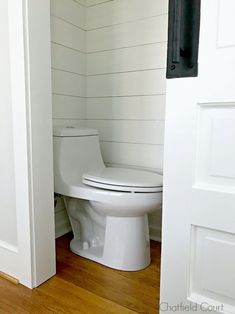 a white toilet sitting inside of a bathroom next to a wooden floor and wall with planks on the walls