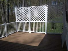 an empty deck with white railings and wood flooring in front of some trees