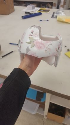 a person holding up a white shoe with pink flowers on the bottom and sides, in front of a workbench