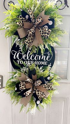 a welcome to our home sign hanging on the front door with green plants and bows