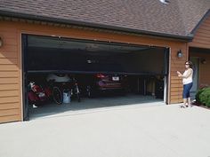 a woman standing in front of a garage with her bike on the driveway and two cars parked inside