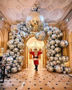 a man dressed as santa clause standing in front of giant silver balls at the entrance to a building