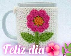 a crocheted coffee mug with a pink flower on the side and green leaves