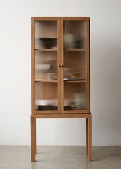 a wooden cabinet with glass doors on the top and bottom shelves, in front of a white wall