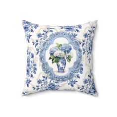 a blue and white pillow with flowers in a vase on the front, against a white background