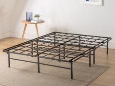 a metal bed frame sitting on top of a wooden floor next to a small table