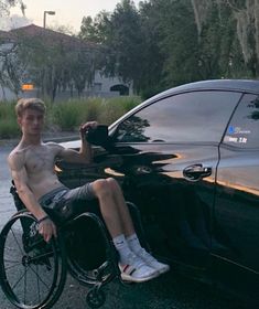 a shirtless man in a wheel chair next to a car