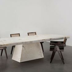 a marble table with chairs around it in an empty room next to a white wall