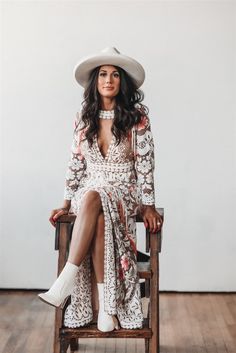 a woman sitting on top of a wooden chair wearing a white cowboy hat and dress