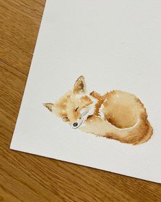 a watercolor painting of a fox laying down on a wooden floor next to a piece of paper