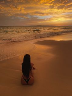 a woman sitting on top of a sandy beach next to the ocean under a cloudy sky