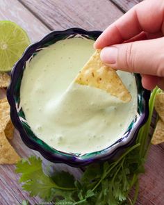 a hand dipping a tortilla chip into a bowl of guacamole