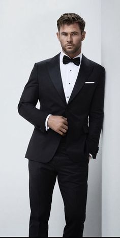 a man in a tuxedo leaning against a wall